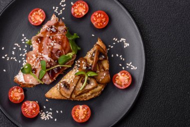 Koyu beton bir zemin üzerinde jambon, mantar ve dana eti, domates ve mikroçerez içeren çeşitli tostlar veya bruschetta çeşitleri