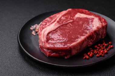 Taze, çiğ biftek, tuz, baharat ve otlar koyu dokulu arka planda.