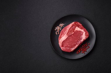 Taze, çiğ biftek, tuz, baharat ve otlar koyu dokulu arka planda.
