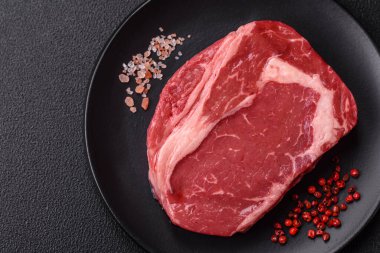 Taze, çiğ biftek, tuz, baharat ve otlar koyu dokulu arka planda.