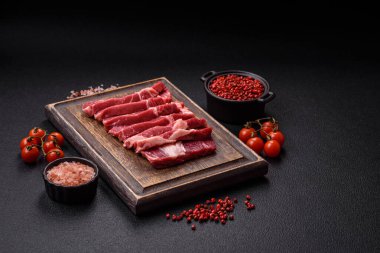 Taze çiğ et, tuzla dilimlenmiş, koyu beton arka planda baharatlar.