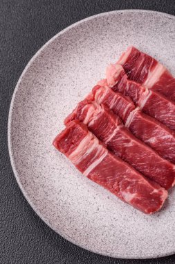 Taze çiğ et, tuzla dilimlenmiş, koyu beton arka planda baharatlar.