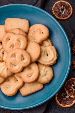 Lezzetli taze, çıtır çıtır tereyağlı kurabiyeler seramik tabakta koyu beton arka planda.