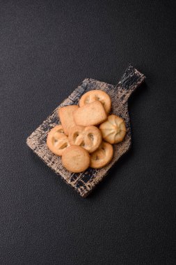 Lezzetli taze, çıtır çıtır tereyağlı kurabiyeler seramik tabakta koyu beton arka planda.