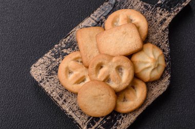 Lezzetli taze, çıtır çıtır tereyağlı kurabiyeler seramik tabakta koyu beton arka planda.