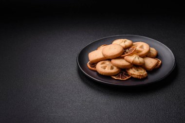 Lezzetli taze, çıtır çıtır tereyağlı kurabiyeler seramik tabakta koyu beton arka planda.