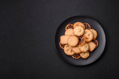 Lezzetli taze, çıtır çıtır tereyağlı kurabiyeler seramik tabakta koyu beton arka planda.