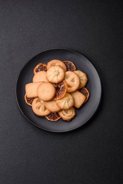 Lezzetli taze, çıtır çıtır tereyağlı kurabiyeler seramik tabakta koyu beton arka planda.