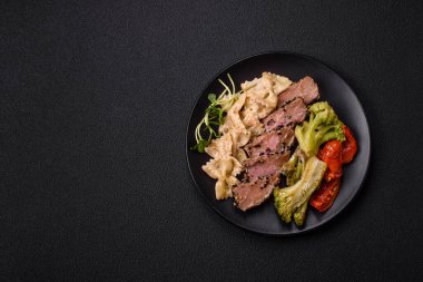 Fırında ton balığı, brokoli, domates ve fusili makarnalı, tuzlu ve baharatlı, koyu beton arka planda.