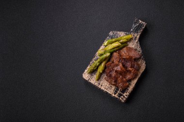 Kaynamış kuşkonmaz, tuz ve baharatla kesilmiş sulu sığır eti ya da domuz eti koyu beton arka planda.