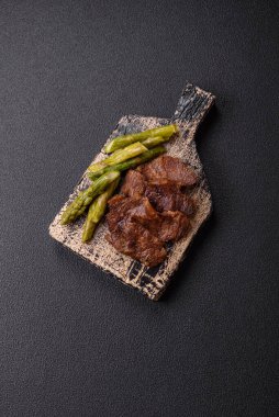 Kaynamış kuşkonmaz, tuz ve baharatla kesilmiş sulu sığır eti ya da domuz eti koyu beton arka planda.