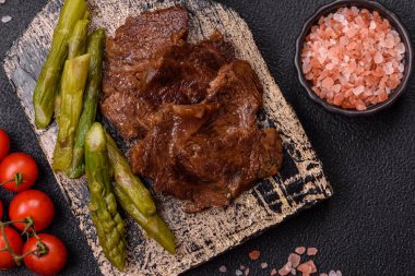 Kaynamış kuşkonmaz, tuz ve baharatla kesilmiş sulu sığır eti ya da domuz eti koyu beton arka planda.