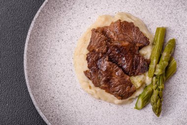 Kaynamış kuşkonmaz, tuz ve baharatla kesilmiş sulu sığır eti ya da domuz eti koyu beton arka planda.