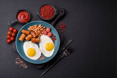 Haşlanmış yumurta, fasulye, sosis, domates, tuz ve baharatlı koyu beton arka planda tam İngiliz kahvaltısı.