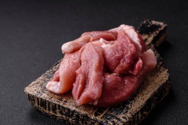 Ahşap kesim tahtasındaki çiğ domuz eti parçaları. Koyu beton arka planda baharatlar ve otlar.