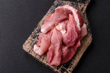 Ahşap kesim tahtasındaki çiğ domuz eti parçaları. Koyu beton arka planda baharatlar ve otlar.