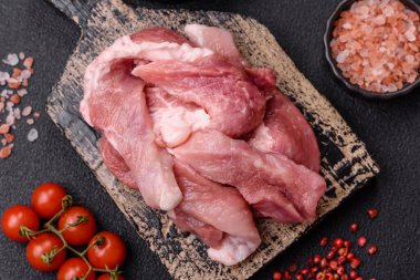 Ahşap kesim tahtasındaki çiğ domuz eti parçaları. Koyu beton arka planda baharatlar ve otlar.