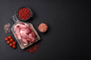 Ahşap kesim tahtasındaki çiğ domuz eti parçaları. Koyu beton arka planda baharatlar ve otlar.