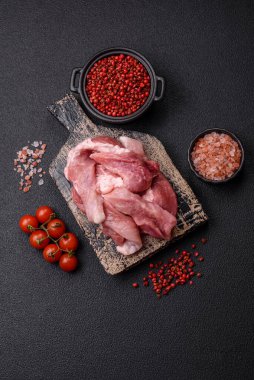 Ahşap kesim tahtasındaki çiğ domuz eti parçaları. Koyu beton arka planda baharatlar ve otlar.