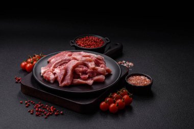 Ahşap kesim tahtasındaki çiğ domuz eti parçaları. Koyu beton arka planda baharatlar ve otlar.