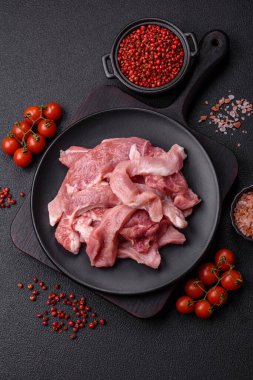 Ahşap kesim tahtasındaki çiğ domuz eti parçaları. Koyu beton arka planda baharatlar ve otlar.