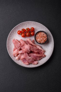 Ahşap kesim tahtasındaki çiğ domuz eti parçaları. Koyu beton arka planda baharatlar ve otlar.