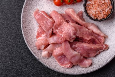 Ahşap kesim tahtasındaki çiğ domuz eti parçaları. Koyu beton arka planda baharatlar ve otlar.