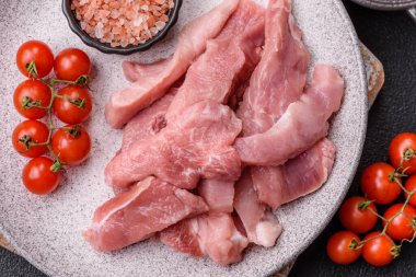 Ahşap kesim tahtasındaki çiğ domuz eti parçaları. Koyu beton arka planda baharatlar ve otlar.