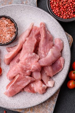 Ahşap kesim tahtasındaki çiğ domuz eti parçaları. Koyu beton arka planda baharatlar ve otlar.