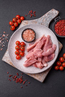 Ahşap kesim tahtasındaki çiğ domuz eti parçaları. Koyu beton arka planda baharatlar ve otlar.