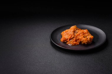 Sliced fish in tomato sauce with salt and spices on a dark concrete background clipart