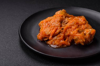 Sliced fish in tomato sauce with salt and spices on a dark concrete background