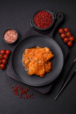 Koyu beton arka planda tuz ve baharatla domates soslu dilimlenmiş balık.