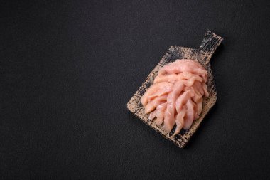 Çiğ tavuk filetosu koyu bir arka planda baharat ve otlarla dilimlenmiş.