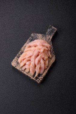 Çiğ tavuk filetosu koyu bir arka planda baharat ve otlarla dilimlenmiş.