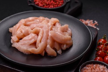 Çiğ tavuk filetosu koyu bir arka planda baharat ve otlarla dilimlenmiş.