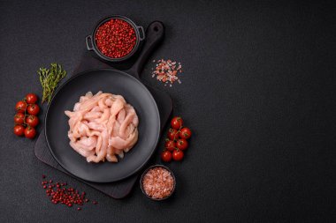 Çiğ tavuk filetosu koyu bir arka planda baharat ve otlarla dilimlenmiş.