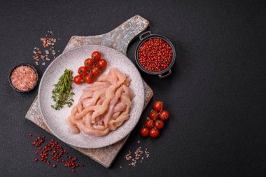 Çiğ tavuk filetosu koyu bir arka planda baharat ve otlarla dilimlenmiş.