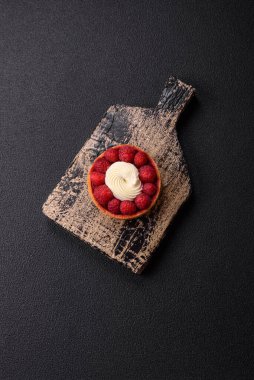 Ahududu ve kremalı tart, koyu dokulu arka planda.