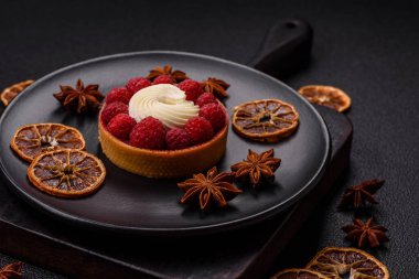 Ahududu ve kremalı tart, koyu dokulu arka planda.