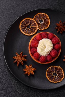 Ahududu ve kremalı tart, koyu dokulu arka planda.