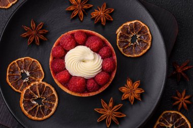 Ahududu ve kremalı tart, koyu dokulu arka planda.