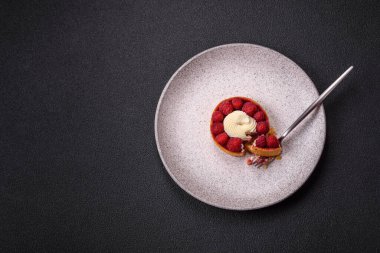 Ahududu ve kremalı tart, koyu dokulu arka planda.