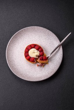 Ahududu ve kremalı tart, koyu dokulu arka planda.