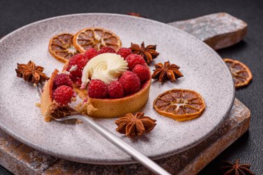 Ahududu ve kremalı tart, koyu dokulu arka planda.