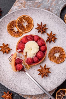 Ahududu ve kremalı tart, koyu dokulu arka planda.