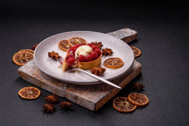 Ahududu ve kremalı tart, koyu dokulu arka planda.