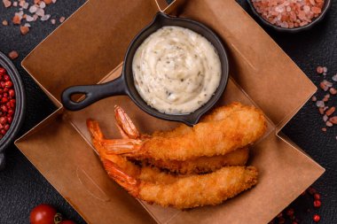 Sıcak gevrek karides, tuzlu ve baharatlı ve beyaz soslu, koyu beton arka planda.