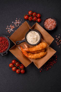 Sıcak gevrek karides, tuzlu ve baharatlı ve beyaz soslu, koyu beton arka planda.