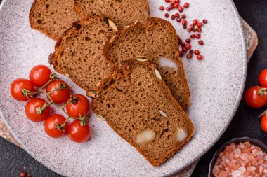 Koyu bir zeminde tohumlu, taneli, tuzlu ve baharatlı kahverengi ekmek.